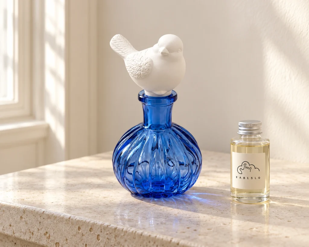 Diffuseur en forme d'oiseau en verre bleu, accompagné d'un flacon de recharge de parfum hermétique, pour une gamme de produits coordonnée.