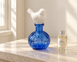 Diffuseur en forme d'oiseau en verre bleu, accompagné d'un flacon de recharge de parfum hermétique, pour une gamme de produits coordonnée.