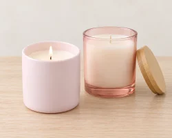 Une bougie en céramique rose pâle allumée, à côté d'un photophore en verre rose pêche muni d'un couvercle en bambou.
